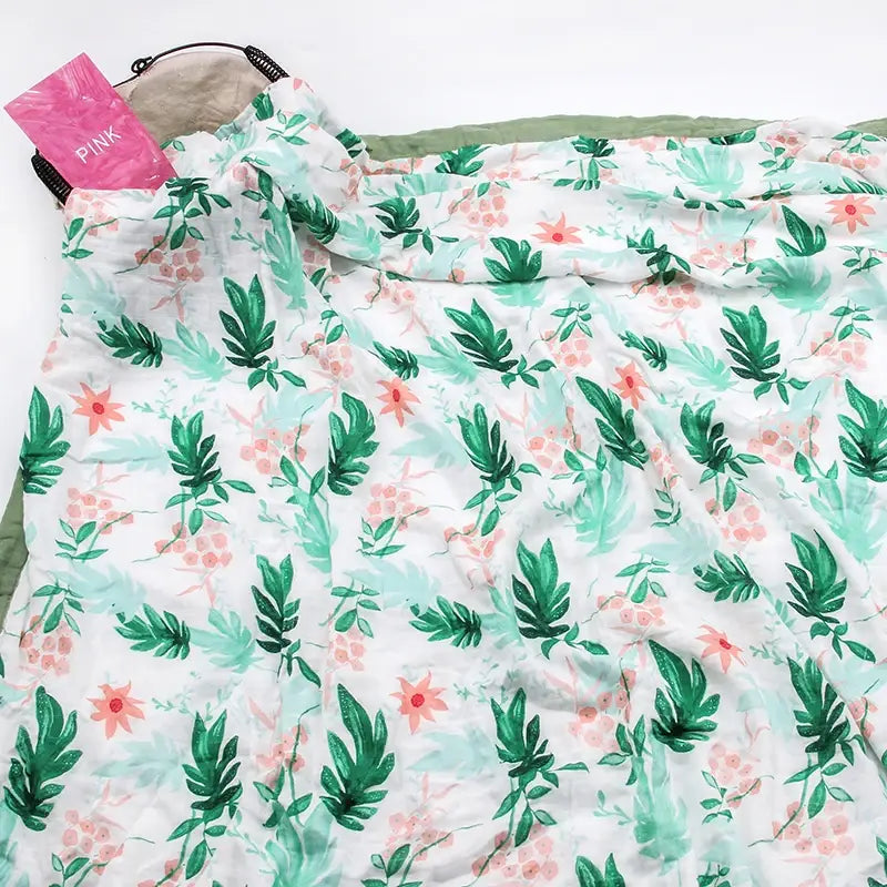 Eine weiche, weiße, gesteppten Bambus-Baumwoll-Decke für Babys (Swaddle) mit floralen Motiven, mit einem lebendigen botanischen Druck aus grünen Blättern und rosa Blumen.