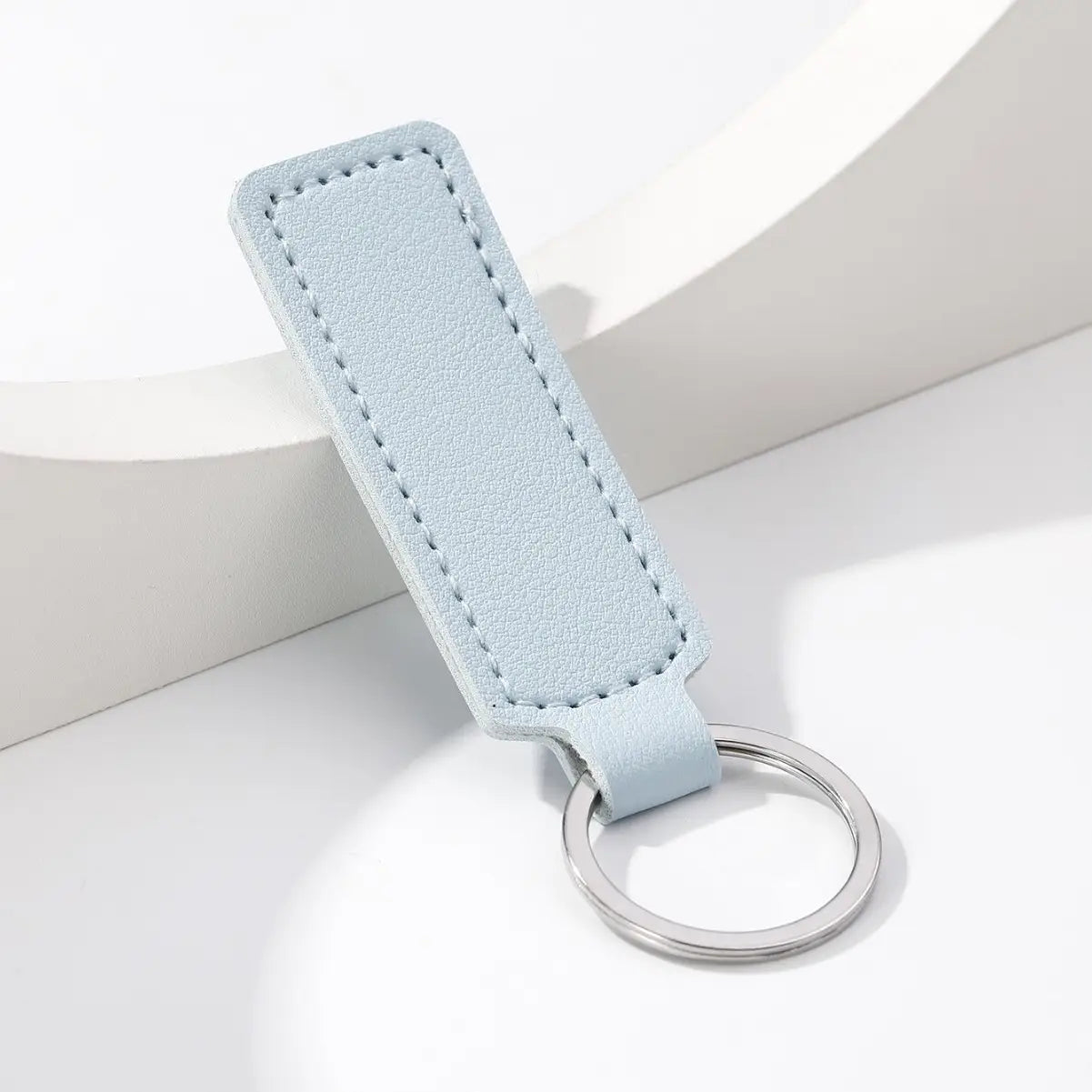 A sleek light blue leather minimalist strip key ring with a silver metal ring designed as a leather car keychain.