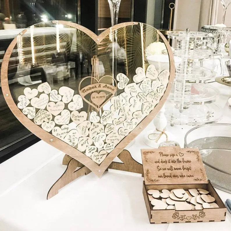 Boîte de dépôt pour livre d’or de mariage en bois, forme de cœur, destinée aux invités, avec un miroir au dos, des initiales gravées et remplie de messages manuscrits sur de petites étiquettes en forme de cœur en bois.