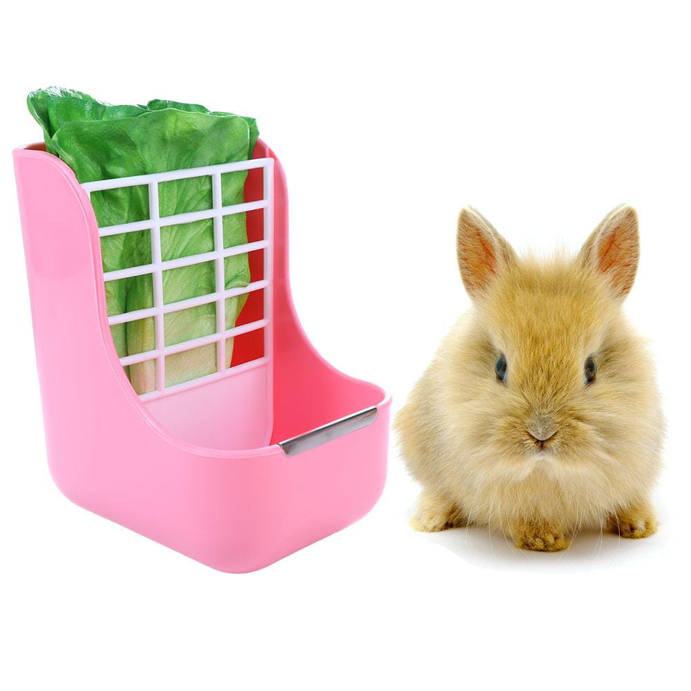 Pink plastic rabbit hay feeder with white grid insert containing green leafy vegetable for small animals with food bowl.