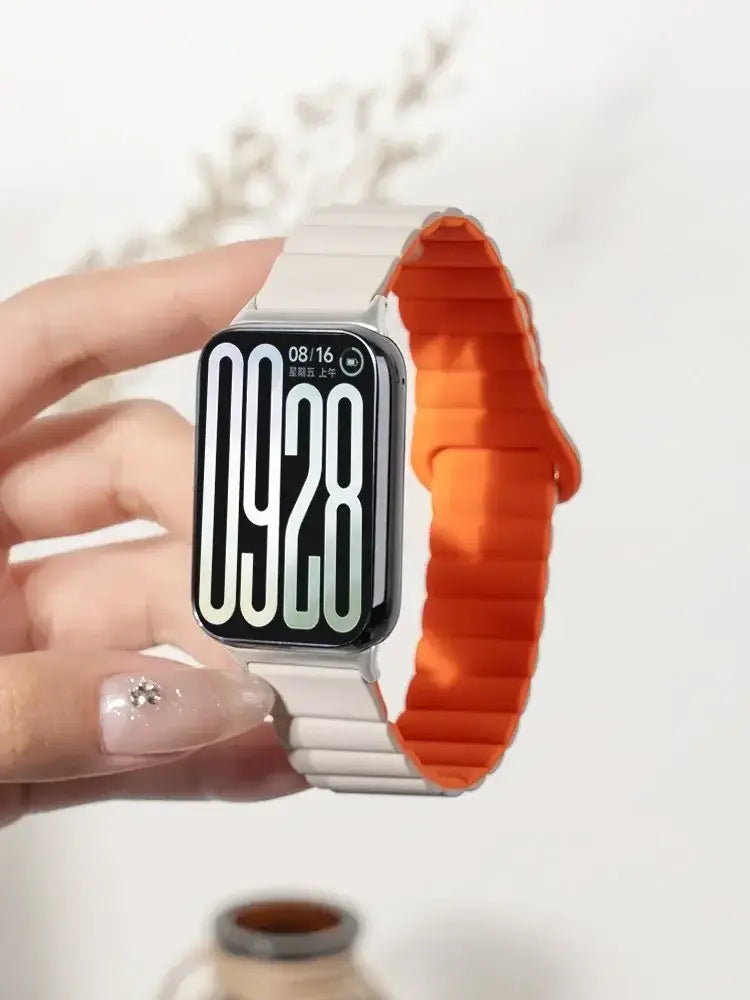 Eine elegante Xiaomi Redmi-Uhr mit einem Silikon-Magnetarmband mit weißem Gliederdesign und leuchtend orangefarbenem Silikon in einer Zweifarben-Optik, die die Uhrzeit und das Datum auf einem schwarzen rechteckigen Display anzeigt.
