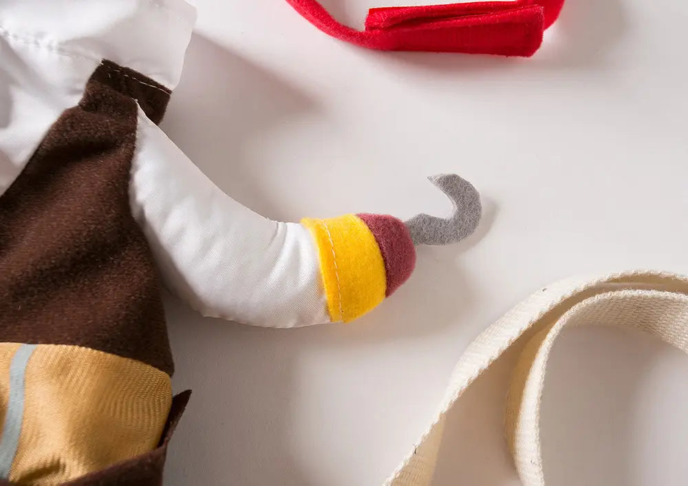 Ein Plüsch-Piratenhaken mit einem gelb- und weinroten gestreiften Griff aus weichem Stoff als Teil eines Piratenhundekostüms mit Hut.