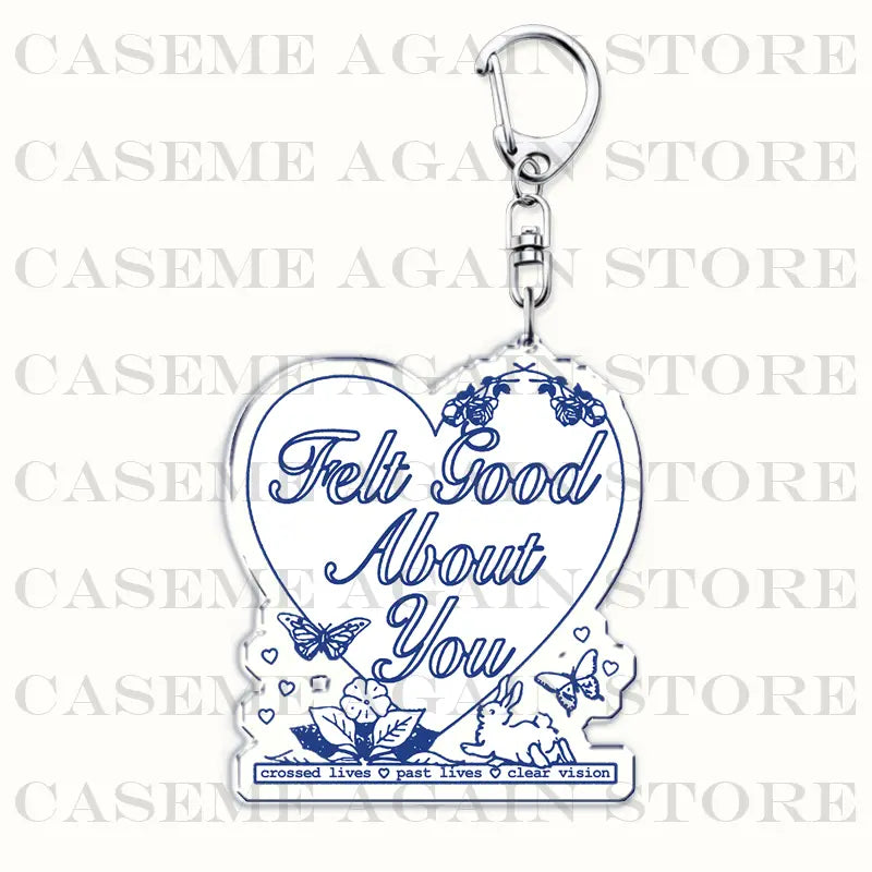 Clear heart-shaped acrylic keychain featuring blue cursive text felt good about you and decorative floral, butterfly, and rabbit illustrations for Gracie Abrams anime fan gift.