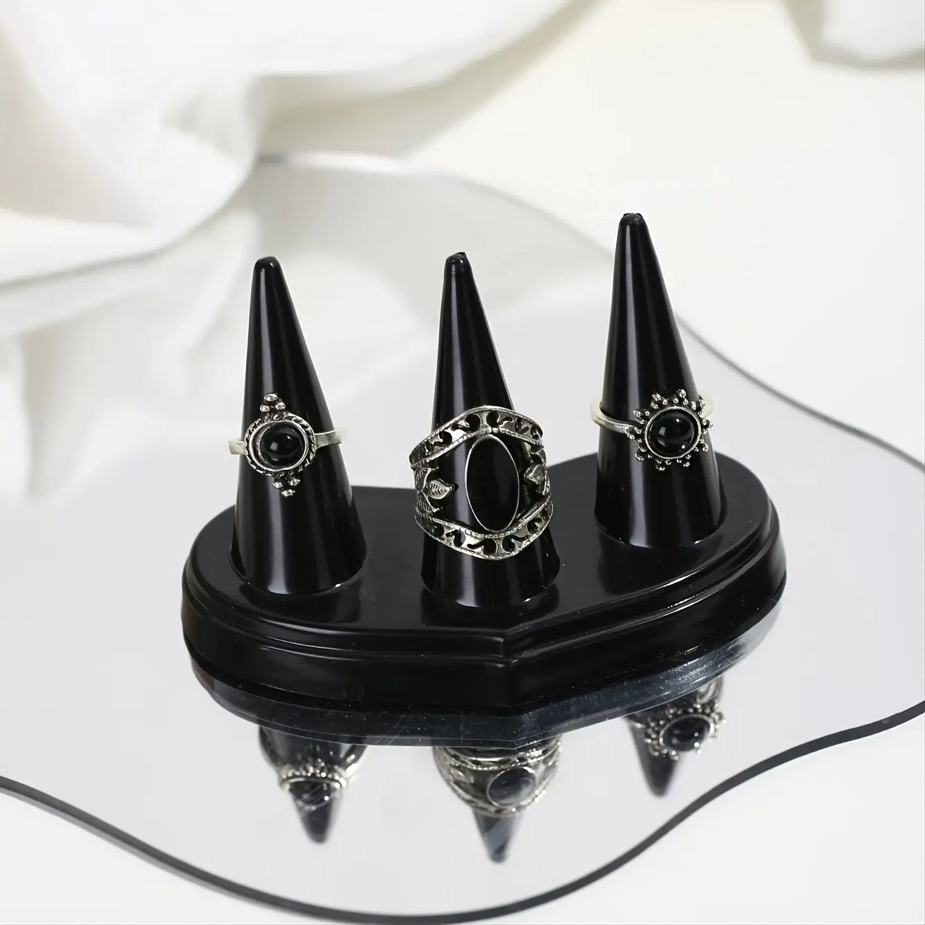 Trois bagues en onyx noir avec des détails en filigrane argentés, présentées sur un support conique en plastique noir lisse à trois supports.