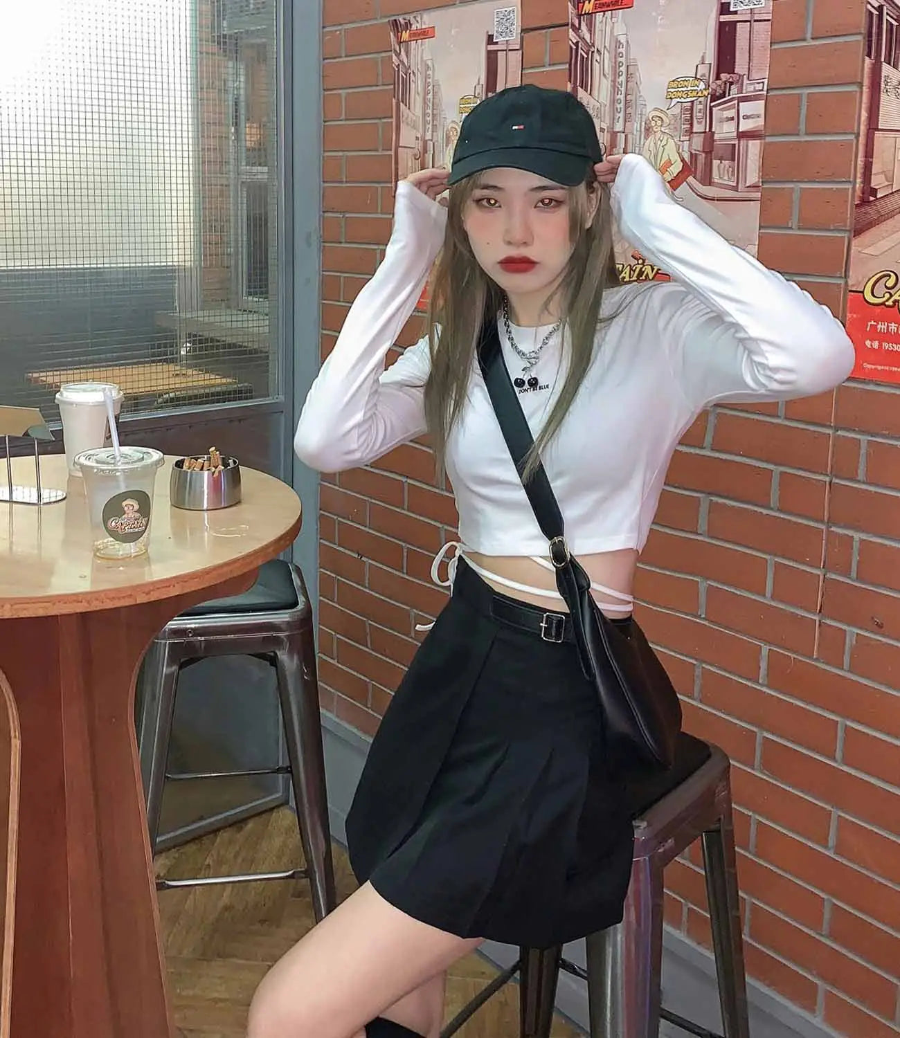 Schwarze Umhängetasche mit Schnallenriemen und weicher Lederoptik, kombiniert mit Damen-Langarm-Crisscross-Crop-Top.