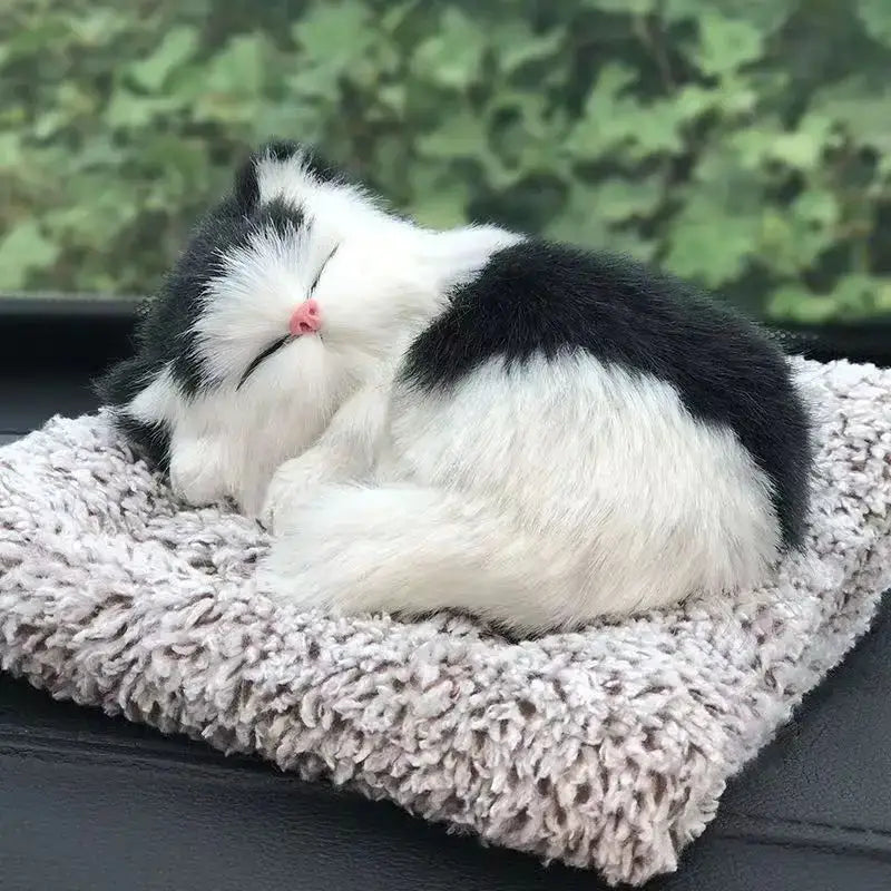 A plush black and white simulated sleeping cat toy with a pink nose curled up on a textured gray cushion featuring sound functionality.