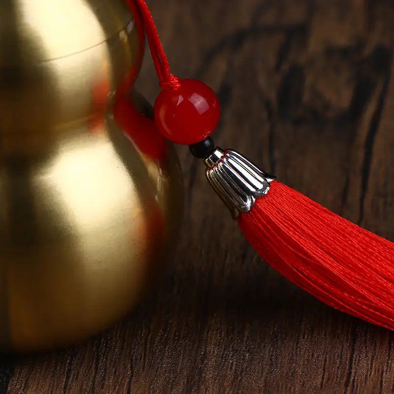 a vibrant red tassel with a glossy jade bead and silver-toned metal cap as part of a brass gourd feng shui prosperity ornament