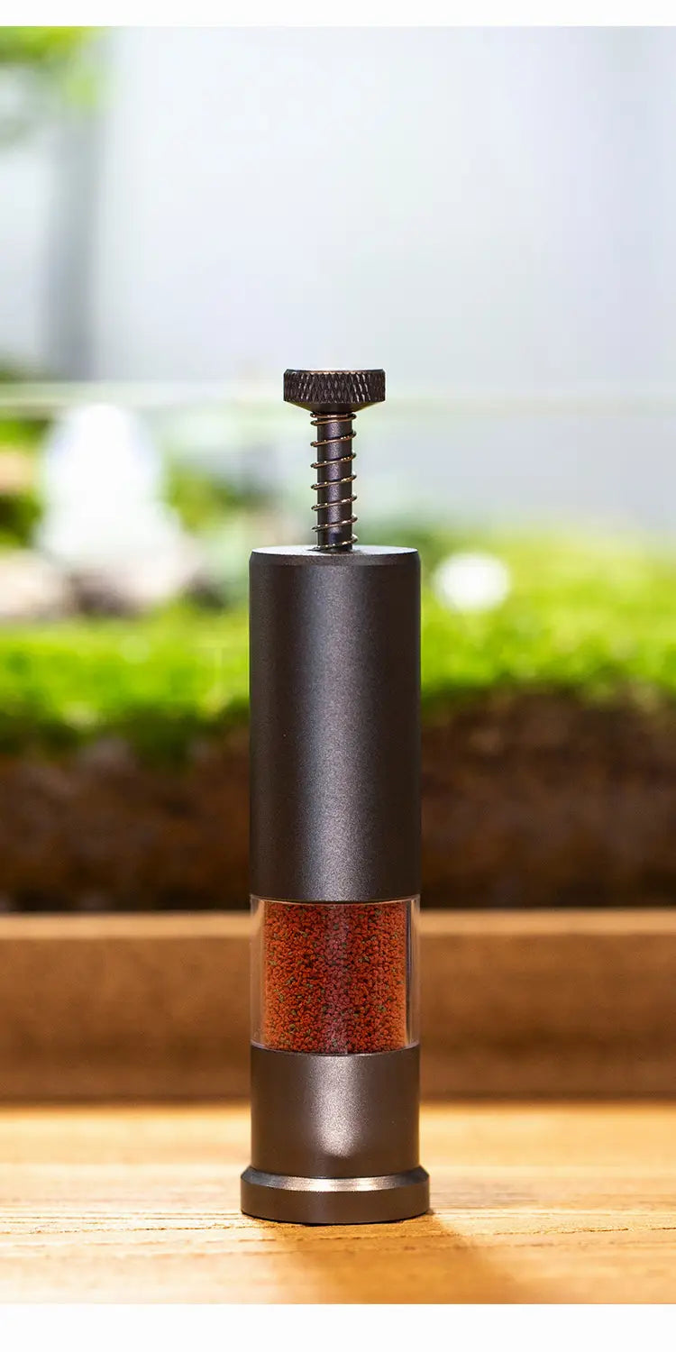 Black metal pepper mill with a textured top knob and clear glass section revealing red peppercorns, designed as a feeder mini aquarium accessories small fish food dispenser.