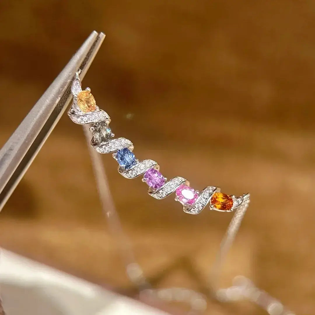 Un délicat collier en argent présentant un design d'oreille pendante en spirale, orné de pierres précieuses en saphir vibrantes orange, bleue, rose et violette, dans une monture pavée.