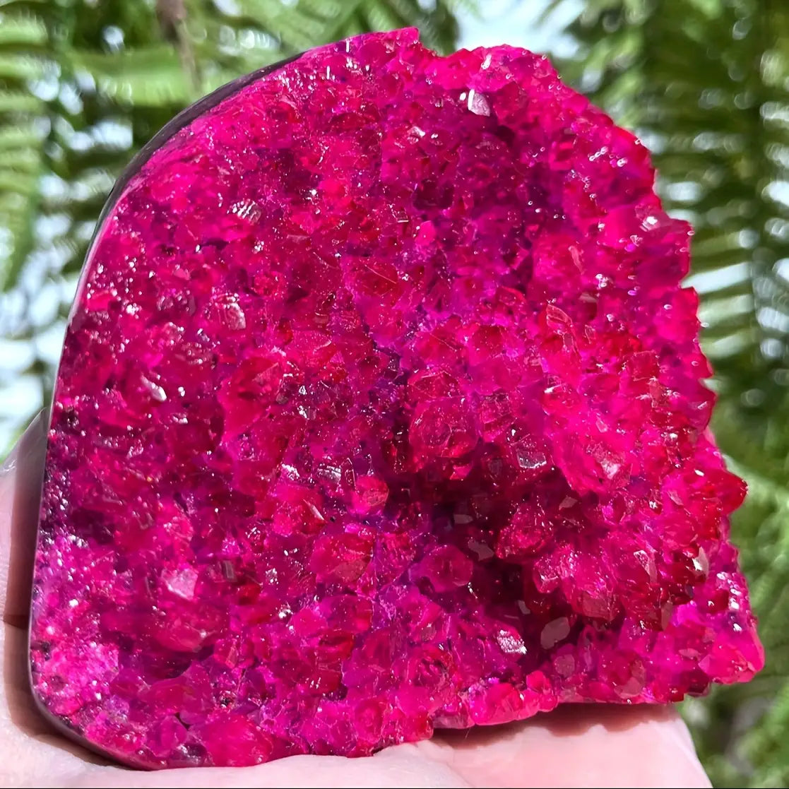 Décoration intérieure pour maison avec un amas de cristaux de géode en quartz rose, mettant en valeur un cristal fuchsia éclatant à la surface brillante et facettée, ainsi que des formations minérales naturelles.