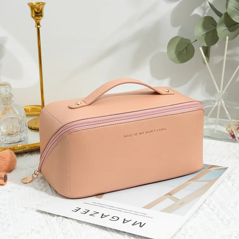 A blush pink leather waterproof travel makeup bag with a top handle and gold-tone hardware embossed with rose of no mans land on the front.