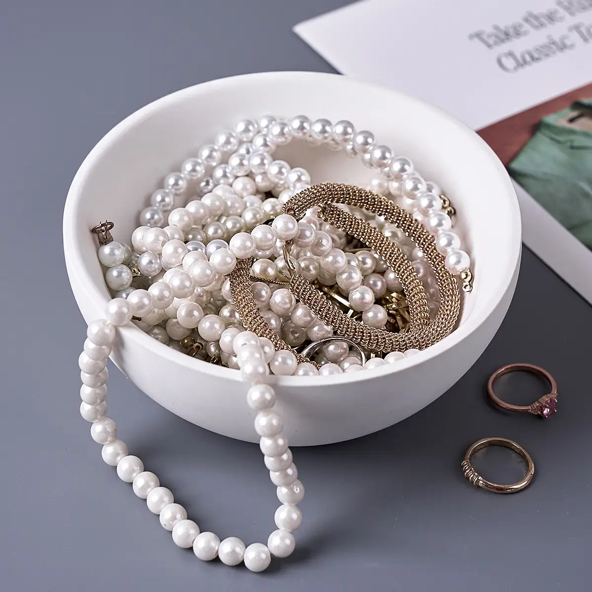 a round silicone mold for making white concrete storage bowls and candles shown with a white ceramic bowl holding white pearls and gold-toned metal jewelry pieces