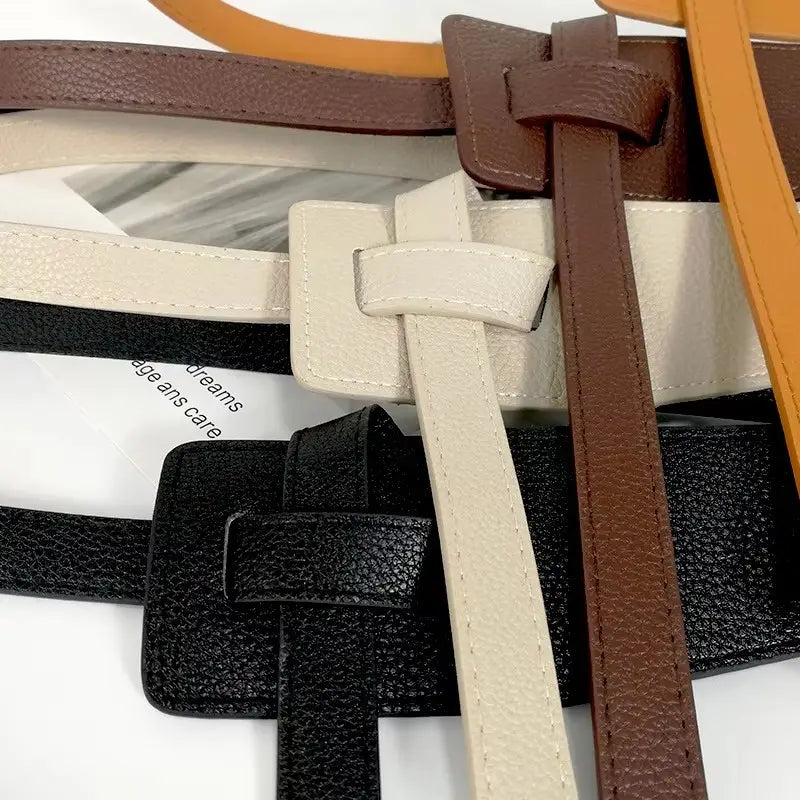 Eine Kollektion von Damen-Gürtelbändern aus weit geschnittenem Kunstleder in Schwarz, Beige und Braun mit strukturierten Oberflächen und passenden rechteckigen Schnallendesigns.