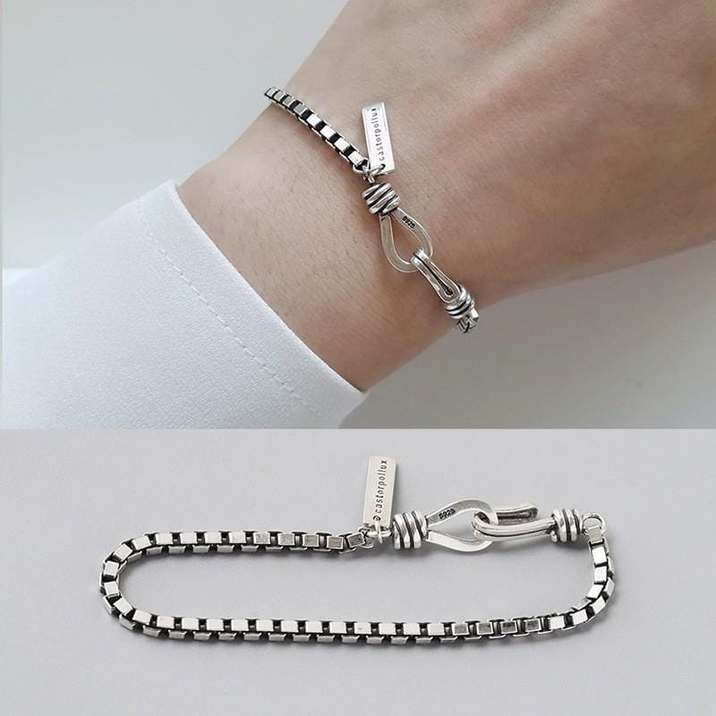 L’image présente un bracelet de charme en métal géométrique à la finition ton argent, en chaîne, pour couples, doté d’une fermeture distinctive de type nœud et d’une plaquette rectangulaire gravée portant le nom de marque cassiopeia