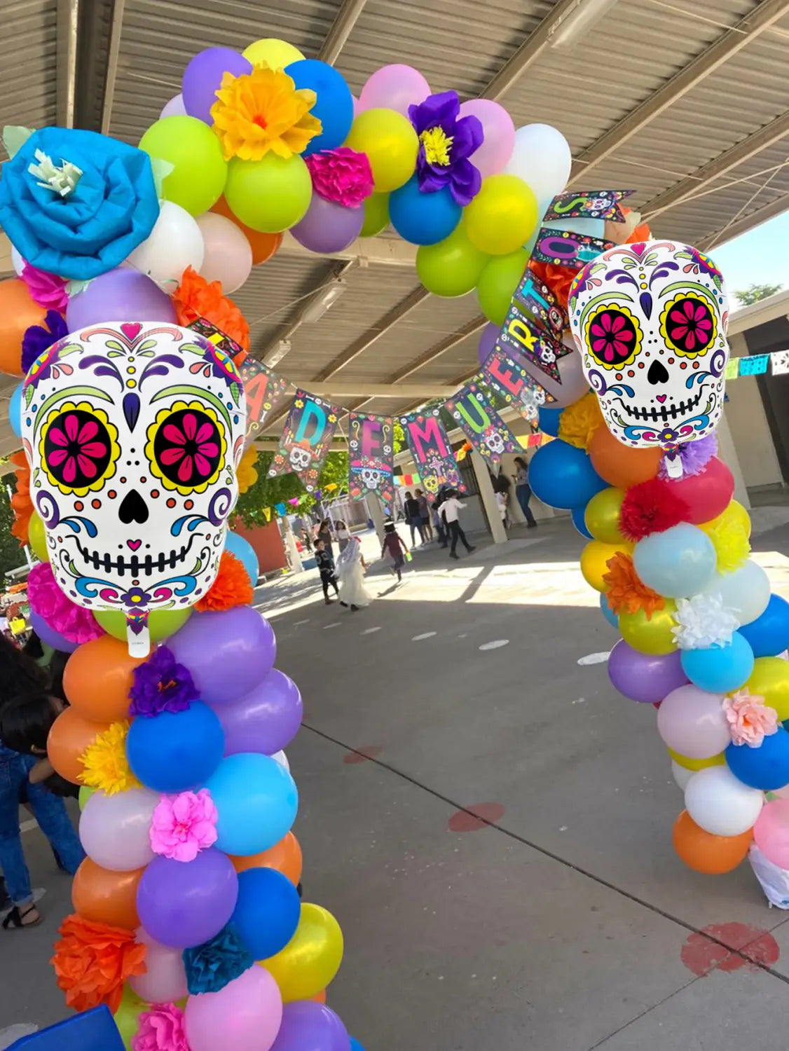 Colorful flower skull foil balloons 3 pack displayed in a vibrant sugar skull balloon arch adorned with colorful balloons and paper flowers.