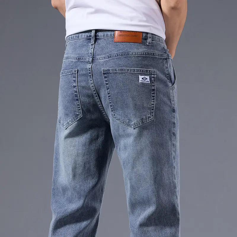 Jeans rétro délavés coupe droite ample pour hommes en denim clair, présentant un design classique à cinq poches et un empiècement de marque en cuir brun sur la ceinture.