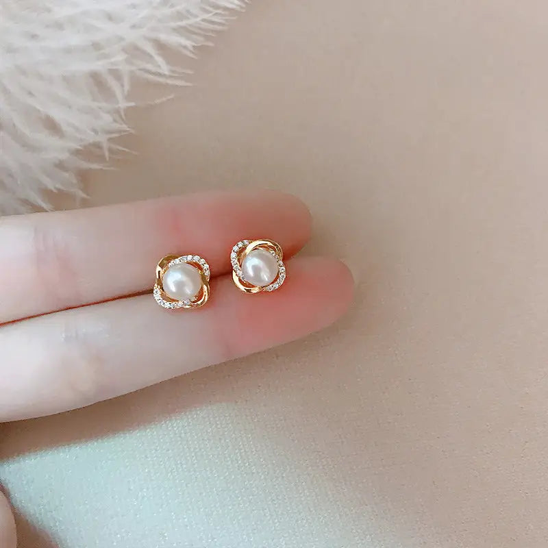 中央のパールをねじれたゴールドトーンの金属フレームで囲み、小さなきらめくストーンをあしらった真珠のツイスト・ゴールドスタッドイヤリング。