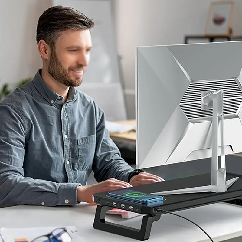 Soporte para monitor de computadora negro con base de carga inalámbrica que ofrece varias opciones de voltaje de puertos de entrada y un diseño moderno y discreto con luz RGB.
