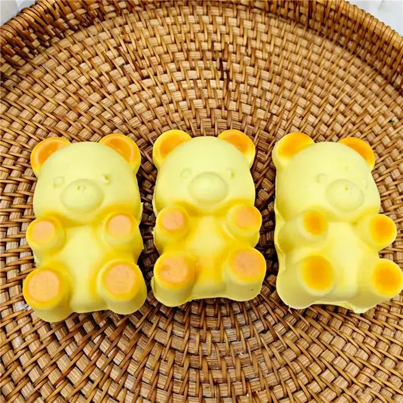 Drei hellgelbe Bärenkopf-förmige Seifenstücke aus langsam aufsteigendem, weichem Knetmaterial für Spielzwecke, mit orangefarbenen Akzenten an Ohren und Pfoten im Hundebrot-Design.