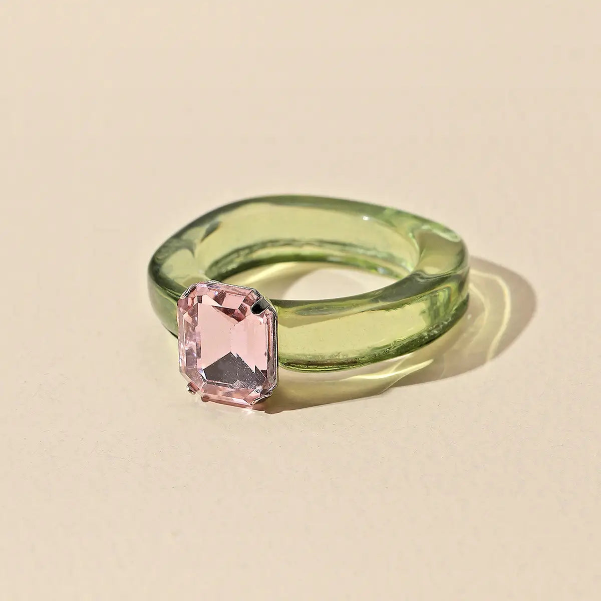 A colorful resin crystal geometric ring for women featuring a translucent green glass band and a prominent pink emerald cut gemstone.