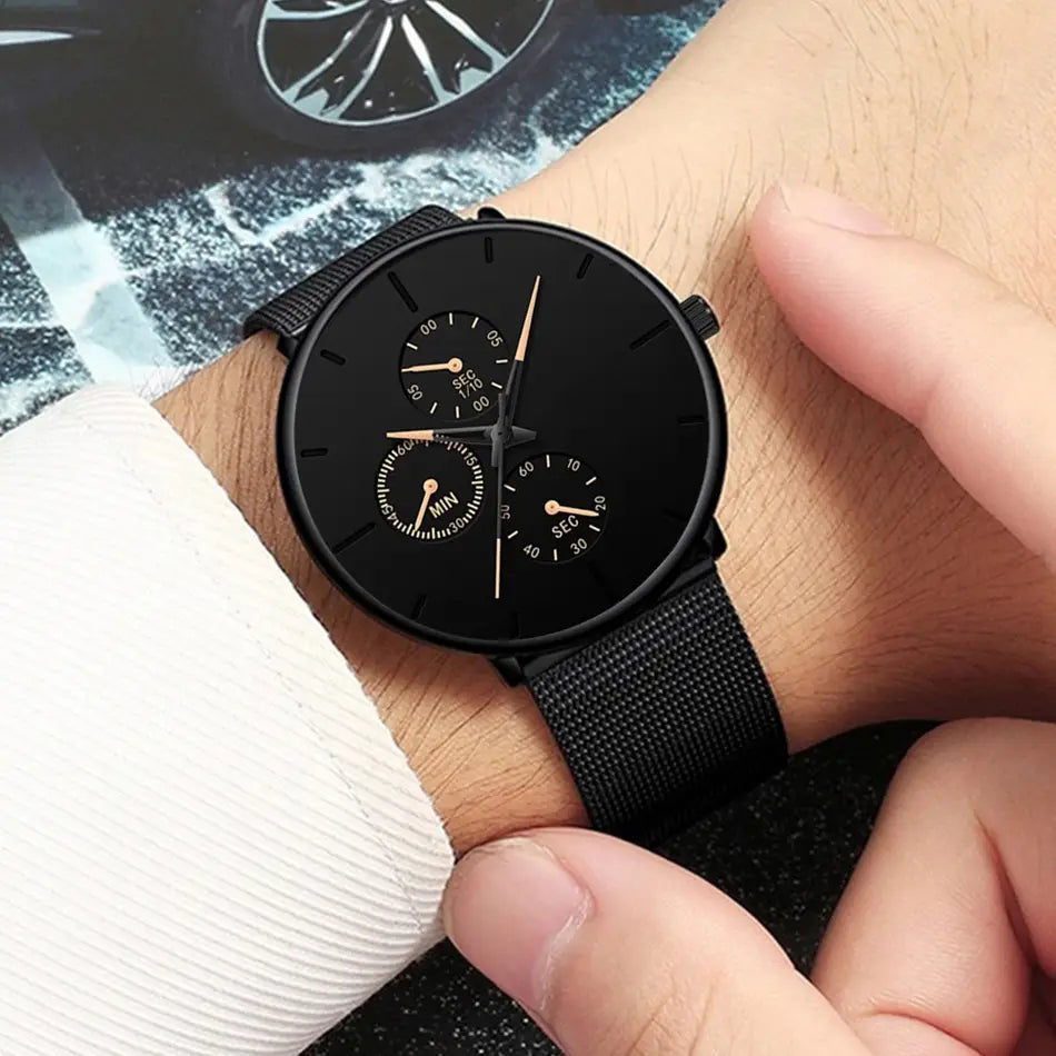 Montre à quartz à maille noire ultrafine pour hommes, avec un design minimaliste, des aiguilles ton or, et trois sous-cadrans pour les secondes, les minutes et les heures.