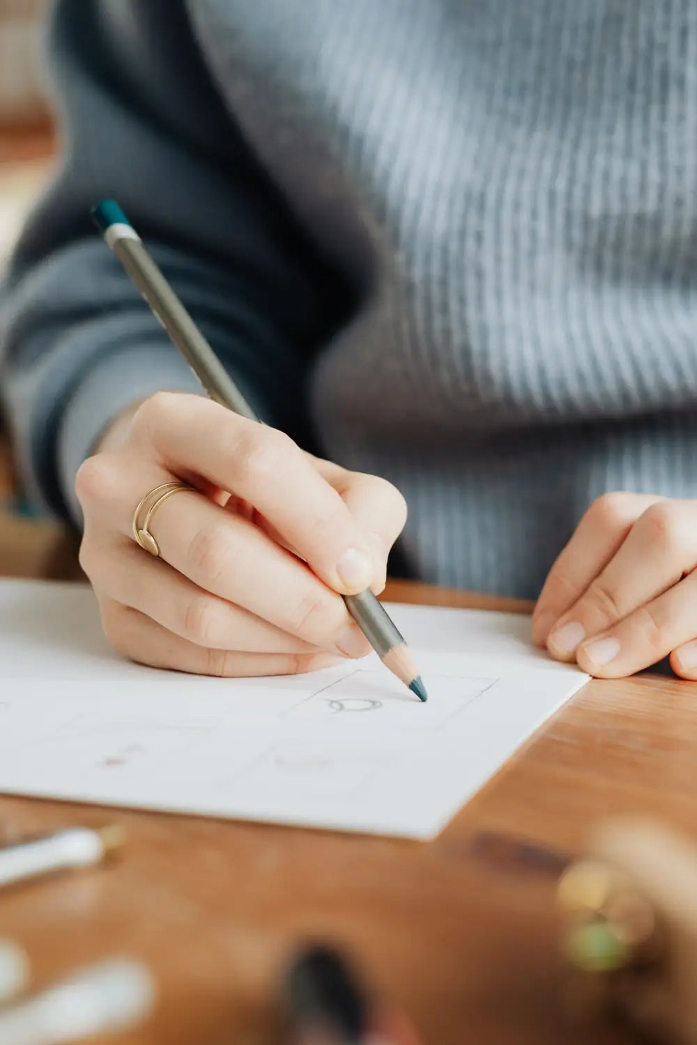 La mano de una persona sostiene un lápiz de grafito con un borrador color verde azulado, preparado sobre papel blanco junto a las fundas universales para asiento de automóvil del juego completo en material negro y color canela.