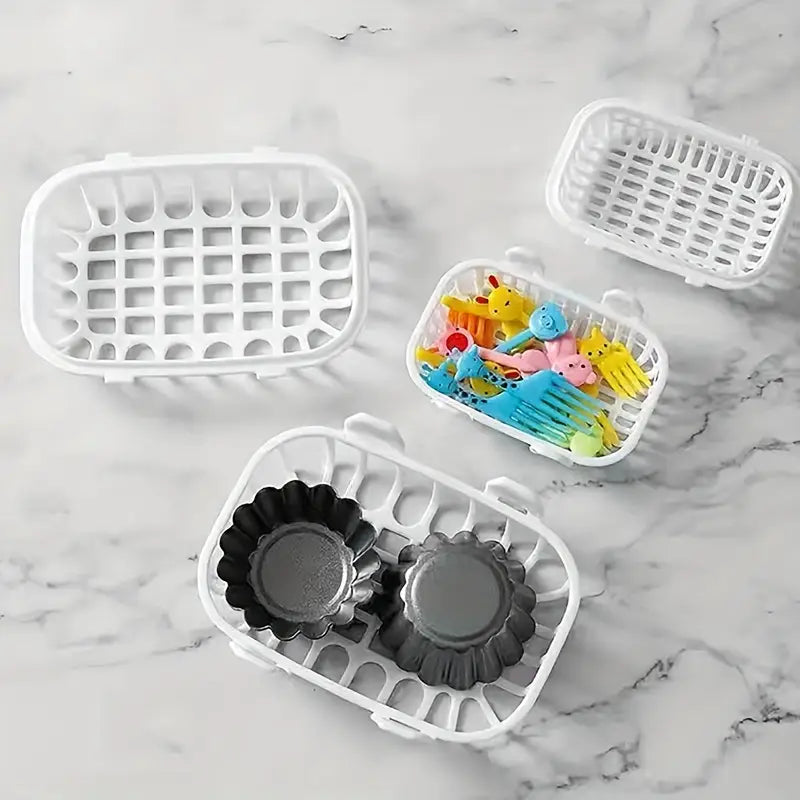 organizador de artículos pequeños en forma de cesta de lavavajillas de plástico blanco con asas de patrón de rejilla: una contiene utensilios de juguete de colores y la otra sostiene dos moldes para hornear negros con forma de flor.