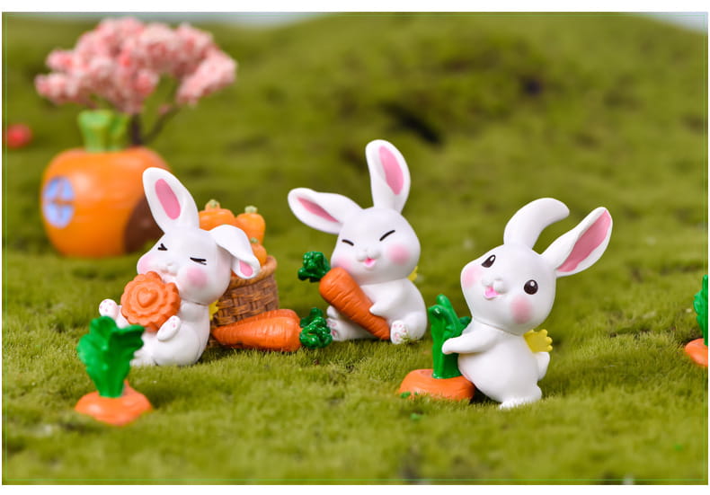 Figurines miniatures en résine céramique blanche de lapin, avec des oreilles internes et des joues roses, tenant ou entourées de miniatures de carottes pour la décoration d’un jardin féerique.