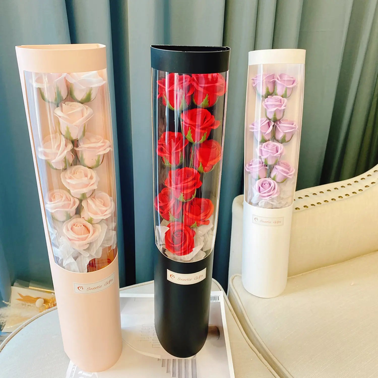Drei zylindrische Glasblumenvase mit konservierten LED-Rosen-Seifenblumen in Pastellrosa, leuchtendem Rot und sanftem Lavendelton in einer Geschenkschachtel zum Valentinstag.