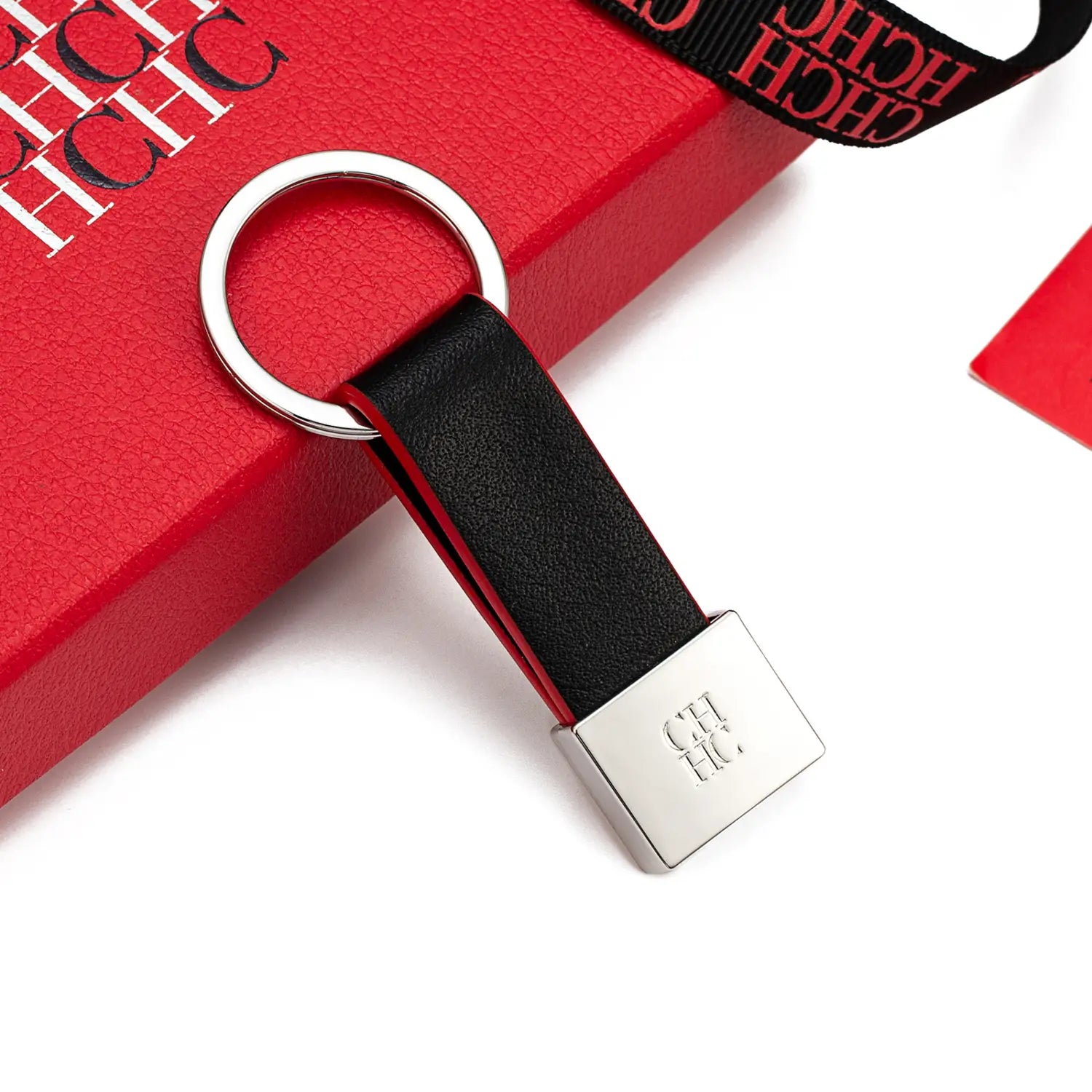 Porta llaves de cuero negro con anillo metálico plateado y placa cuadrada con el logotipo hch grabado, diseñado como accesorio de equipaje minimalista.