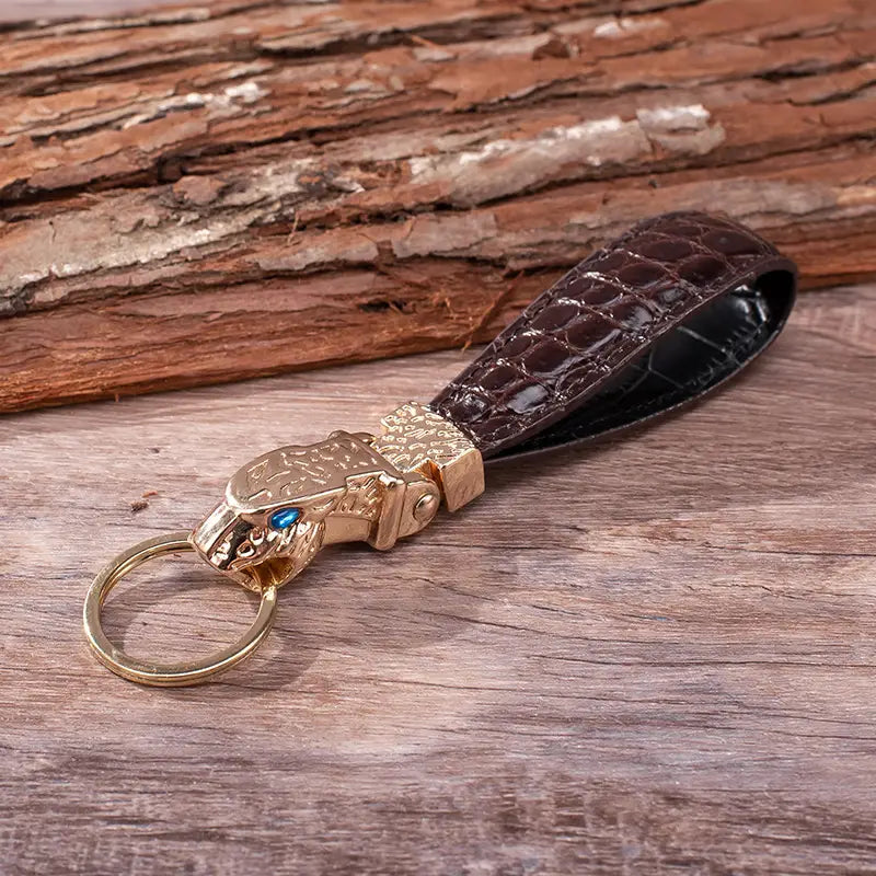 Brown crocodile-patterned leather keychain with a gold-toned tiger head charm featuring an embedded blue gemstone for use as a luxury car key ring.