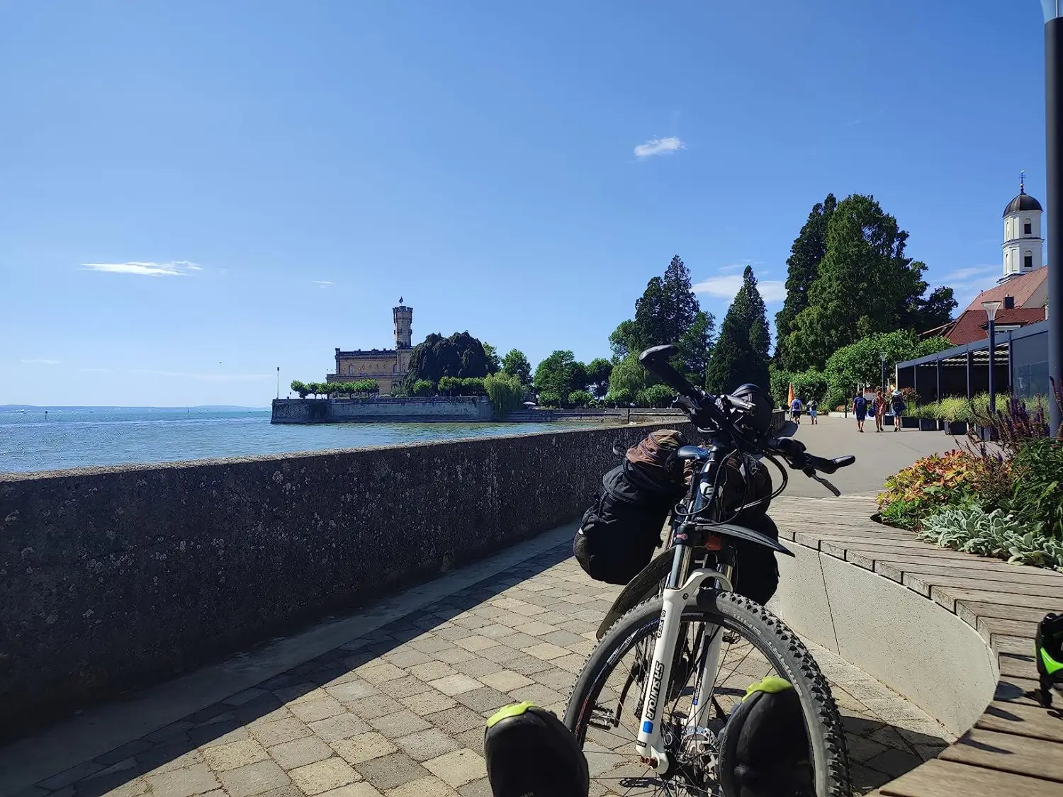 Schwarzes Mountainbike mit Vorderradfederung, neben einer Steinmauer abgestellt, mit Blick auf das Wasser; zeigt die schwarze Ztz 50l wasserfeste Doppelfahrradtasche auf dem hinteren Gepäckträger.