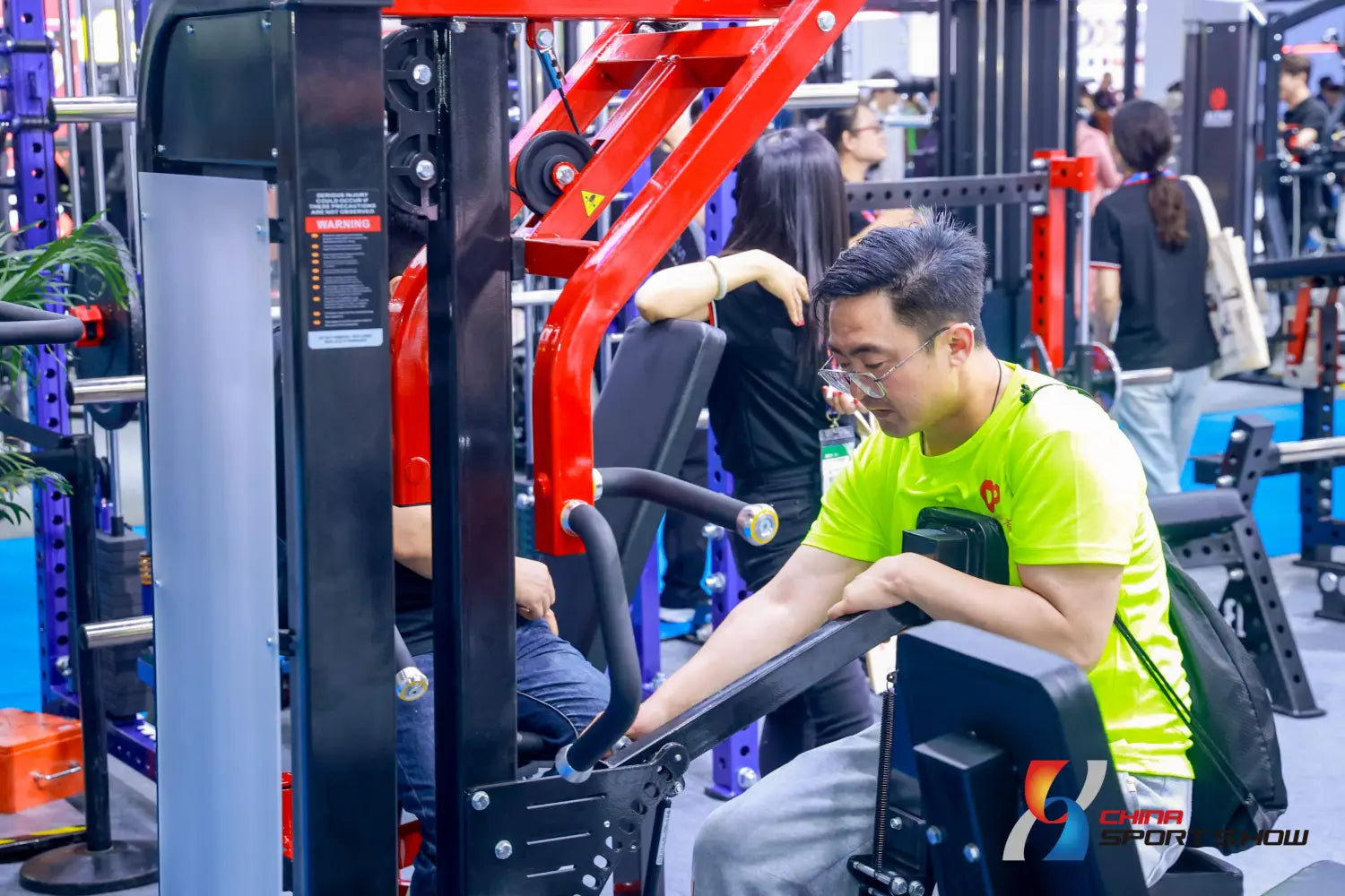 A man in a bright neon green t-shirt is seated on a red and black commercial stair climber machine cardio stepmill in an indoor gym.
