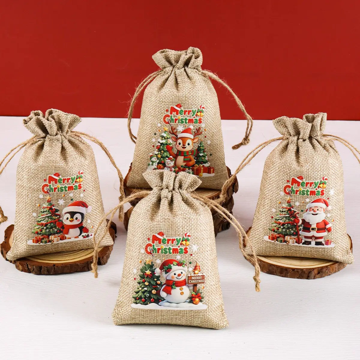 Sachets cadeaux en jute beige à cordon coulissant, lot de 6, avec des illustrations festives de Noël du Père Noël, d’un pingouin et d’un bonhomme de neige, avec un texte Joyeux Noël.