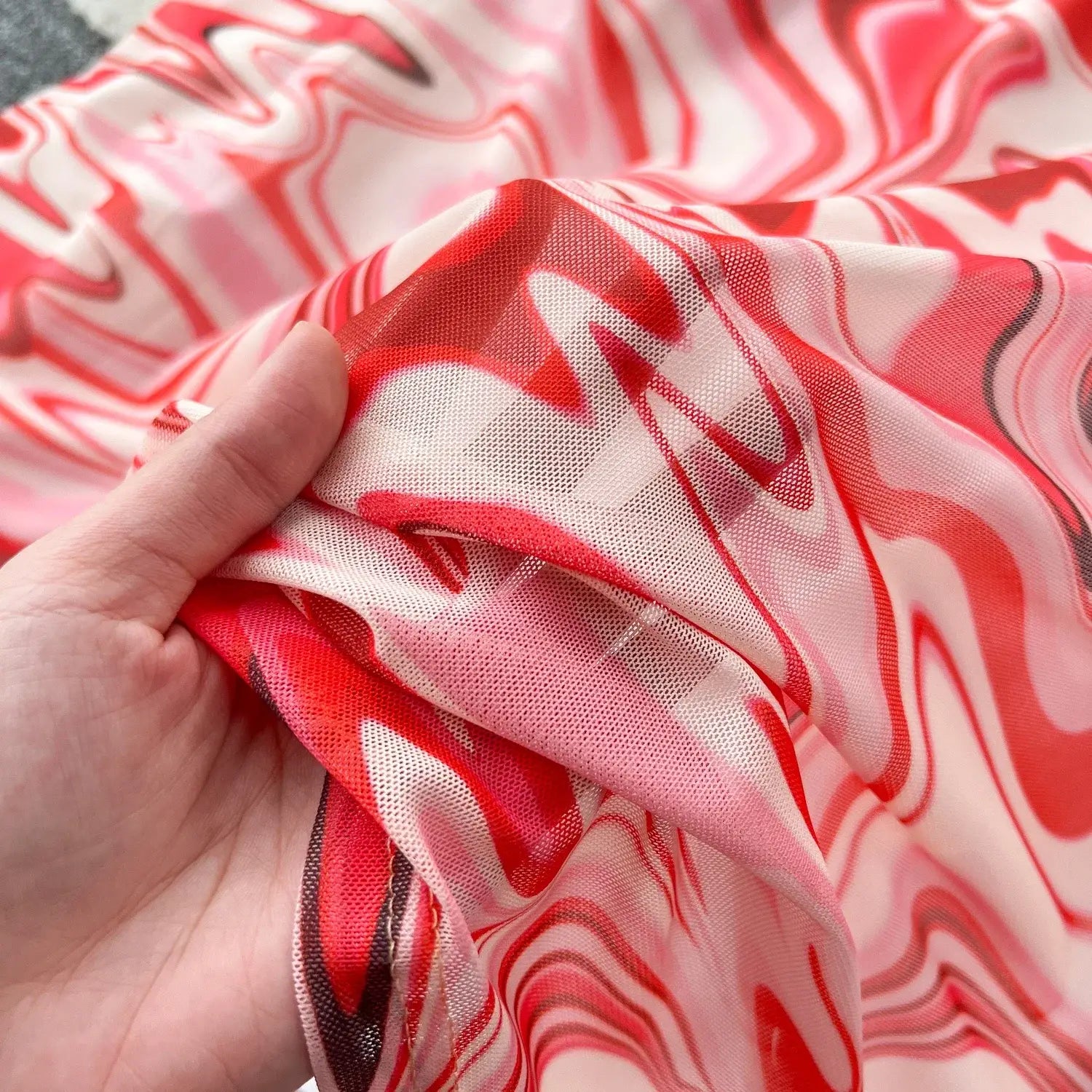 a delicate semi-transparent scarf with a vibrant red and white marbled pattern paired with a two piece mesh skirt set featuring a marble print and elastic closure type