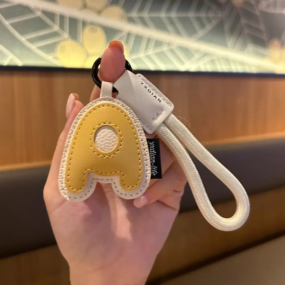 Yellow leather initial keychain letter wristband charm featuring a letter A with white stitched edges and a matching braided strap.