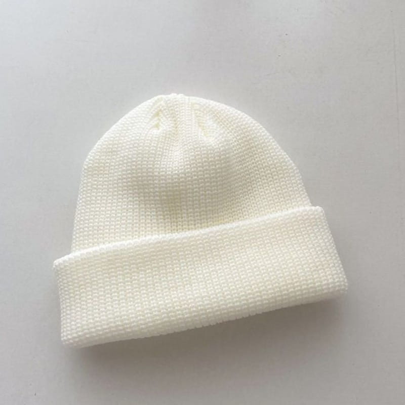 A soft white ribbed knit winter beanie hat with a folded cuff made of warm material designed for unisex use.