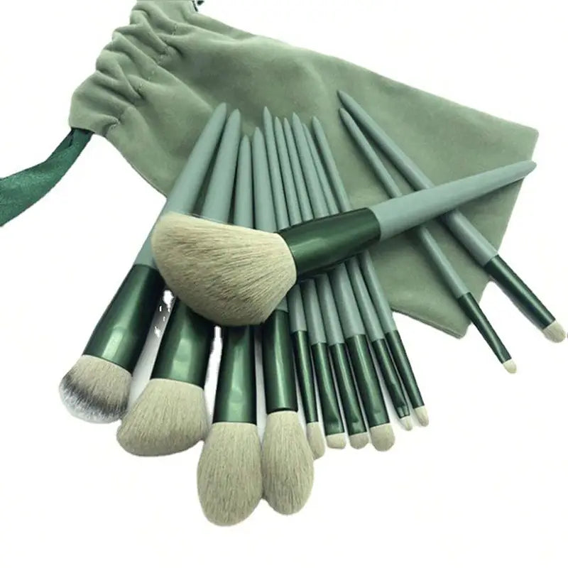 Set aus 15 professionellen Make-up-Pinseln mit eleganten grünen Griffen und weichen hellbeigen Borsten, angeordnet vor einem passenden salbeigrünen Samtbeutel.
