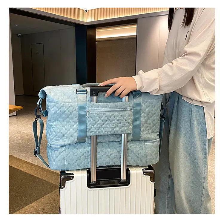 Bolsa de viaje tipo duffel acolchada azul claro con bolsillo frontal y asa retráctil, diseñada para su uso como tote weekender grande.