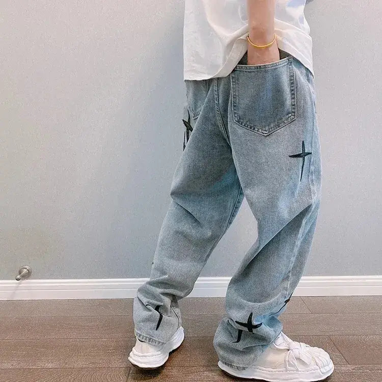 Jeans en denim délavé clair ample à jambes larges, avec broderie croisée noire sur les cuisses et les revers