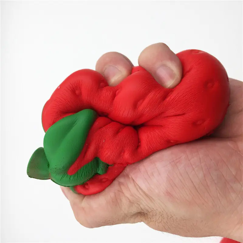Bola antiestrés blanda de silicona con forma de pimiento rojo y verde, mostrada desde el lado posterior, como un juguete antiestrés de fresa gigante, que se eleva lentamente y es blandamente esponjoso.