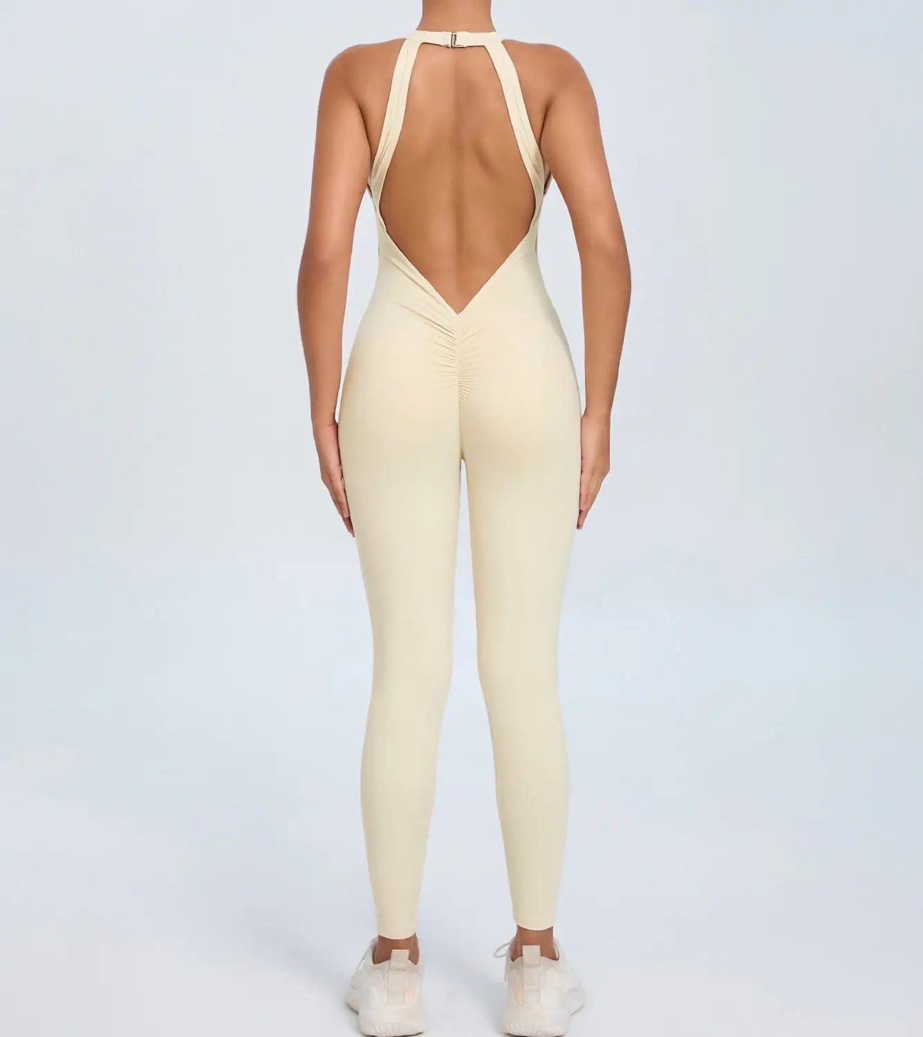 cream-colored form-fitting one-piece athletic jumpsuit with a halter neckline and an open back design shown from the back for workout use