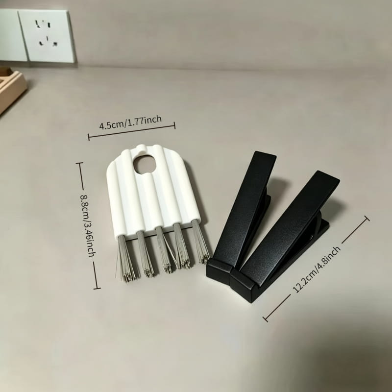 white plastic and metal keyboard cleaning brush with multiple bristles alongside two black plastic clips from a keyboard stand and cleaning brush set