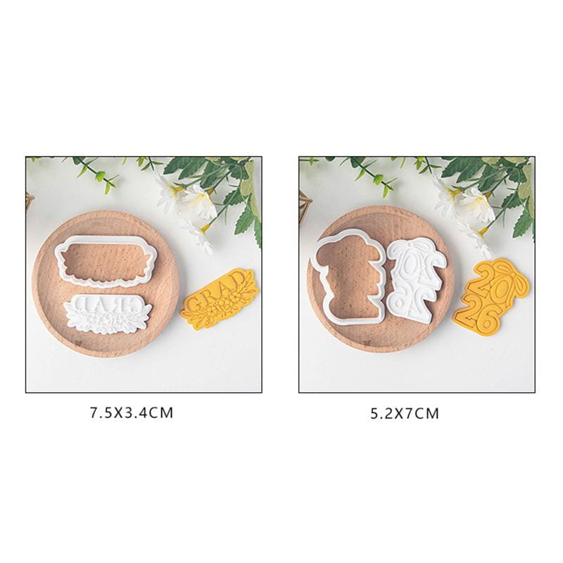 White plastic graduation-themed cookie cutters including a grad banner and the year 2026 displayed on wooden plates from the 2026 graduation cookie cutter set.