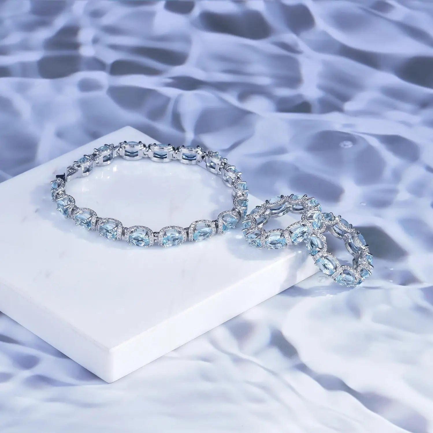 A pair of elegant silver-toned bracelets with oval-cut light blue aquamarine crystals in a delicate sparkling bridal jewelry set.