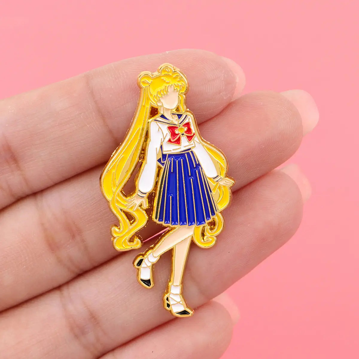 「セーラームーン」猫のエナメルピンセットより、長いブロンドの髪を持ち、青いセーラー服と赤いリボンを身に着けた「セーラームーン」キャラクターをあしらったゴールドのエナメルピンです。