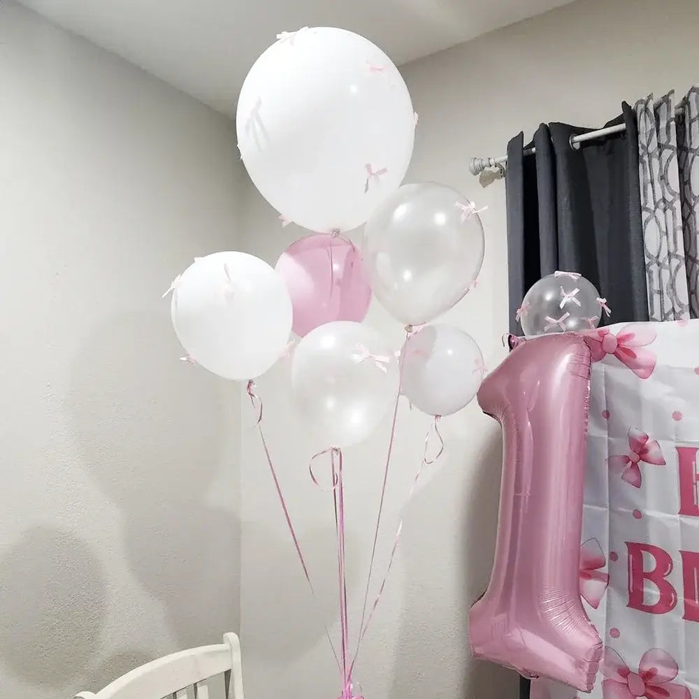 Un ballon métallique rose brillant représentant le chiffre un, faisant partie d’un ensemble de ballons à nœud blanc avec des rubans roses, pour la décoration de fête.