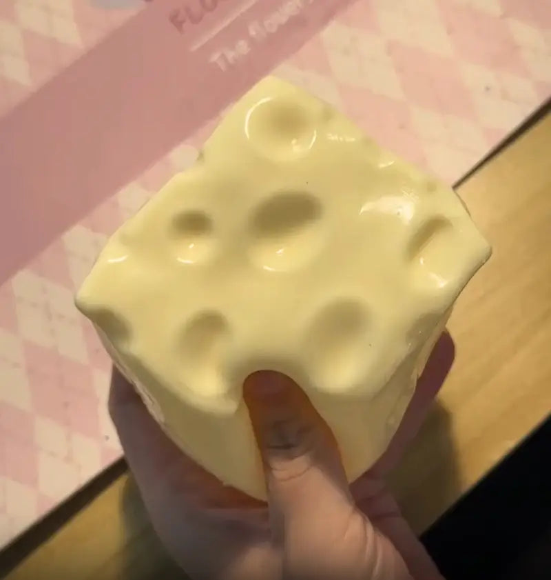 Un jouet à mâcher et à malaxer en forme de carré de fromage jaune pâle, à finition brillante et avec des orifices caractéristiques, conçu pour soulager le stress et apaiser le stress lié au jouet.