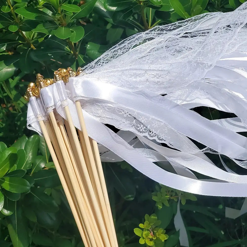 鈴付きのホワイトリボン結婚式用の振り棒（白いレースとサテンリボンをあしらい、ゴールド仕上げの木製ハンドルが付いたブーケスティック）。20本セット