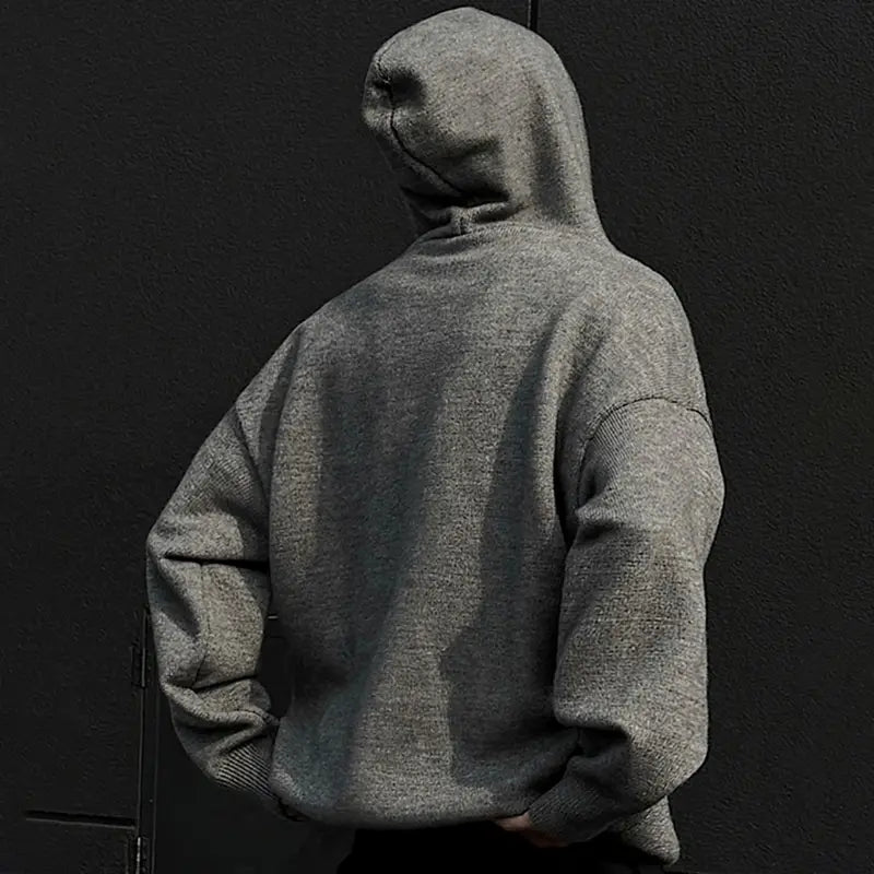 Eine Person in einem melange-grauen übergroßen Strickpullover mit Kapuze mit gerippten Bündchen und Saum, dargestellt als Herren-übergroßer Strickpullover mit Kapuze im Retro-Streetwear-Pullover-Stil.